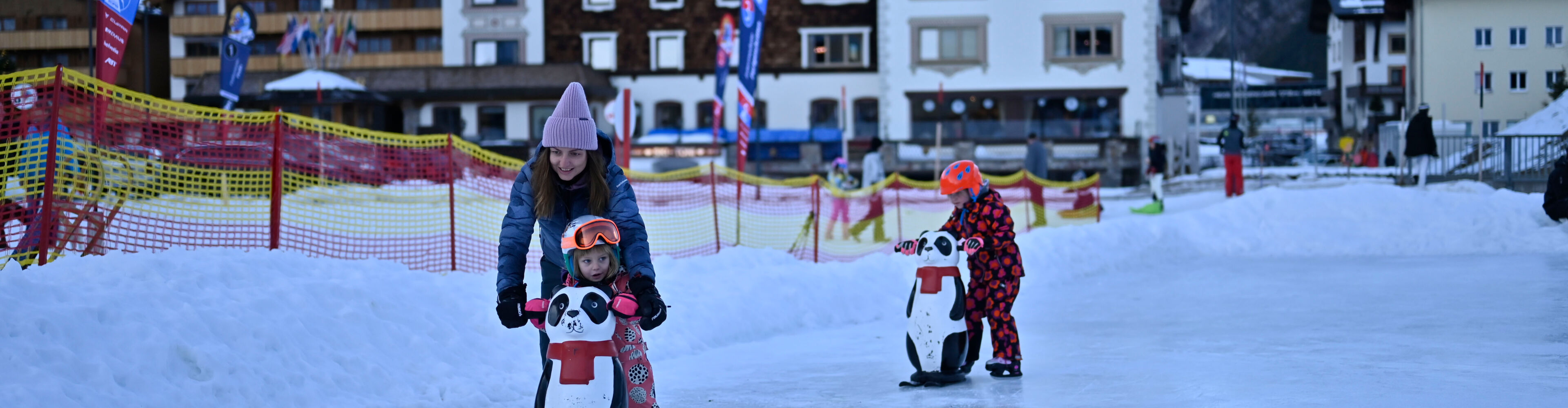 zwei Kinder fahren mit einer Eislaufhilfe Schlittschuhe auf dem Eislaufplatz in Zürs