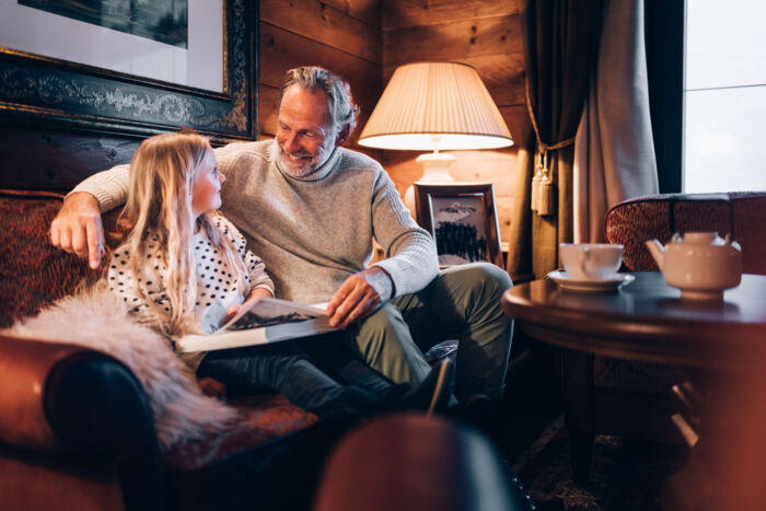 Großvater und Enkelin sehen sich im Familienurlaub gemeinsam Bilder auf dem Sofa an